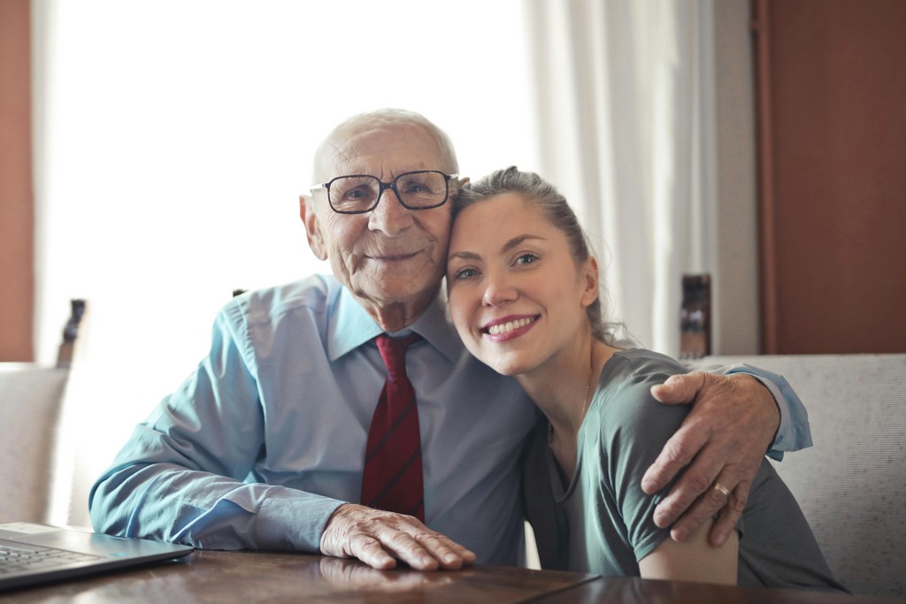 An old man and a young woman embrace and smile.