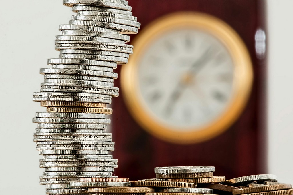 A large clock waes over a pile of coins.