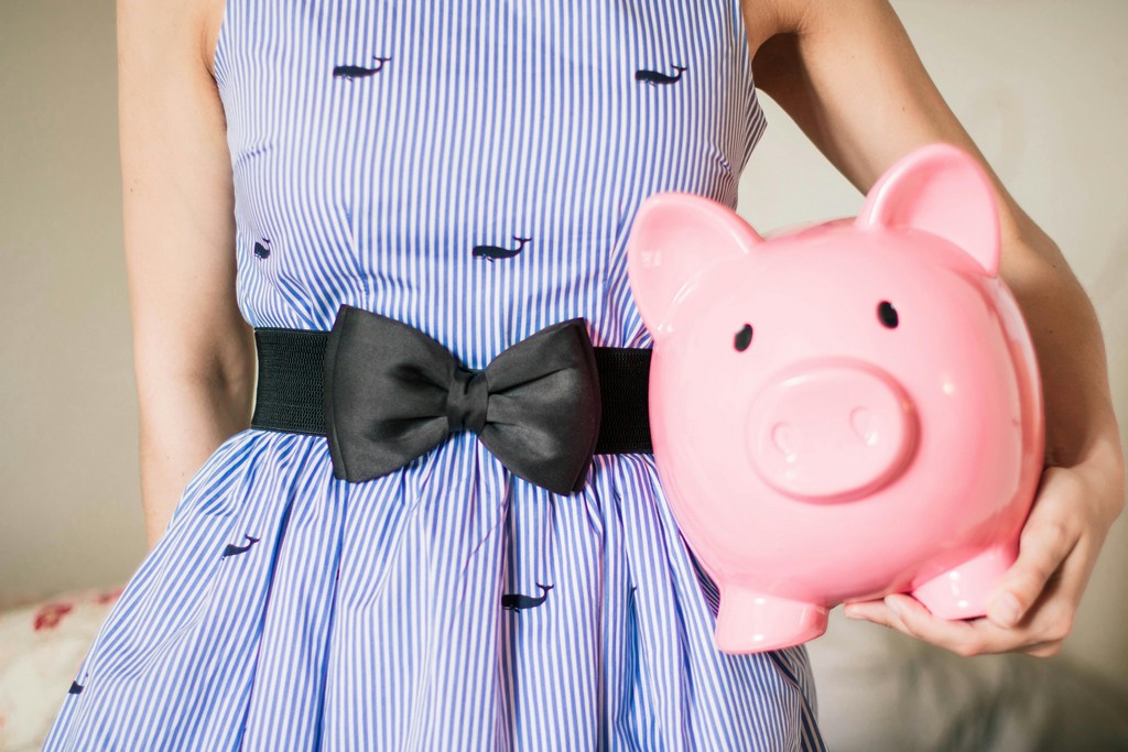 A woman in a blue dress holds a large piggy bank.